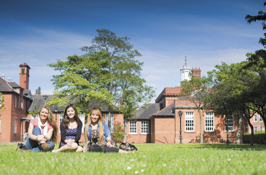 Three students sitting on the grass in front of INTO Manchester
