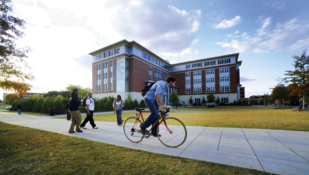 A male University of Alabama at Birmingham student riding a bicycle through campus