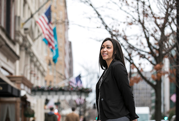 A woman in a dark blazer stands in front of a Washington, DC city block.