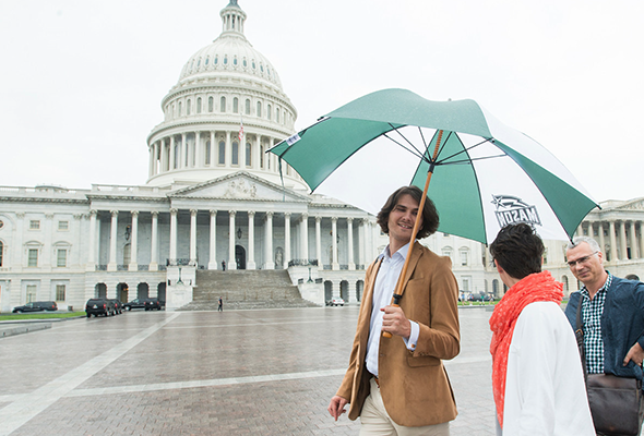 A group of people holding a Mason-branded umbrella stand in front of the US capitol building.