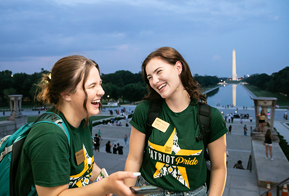 Two Mason students stand in front of the Washington Monument. 